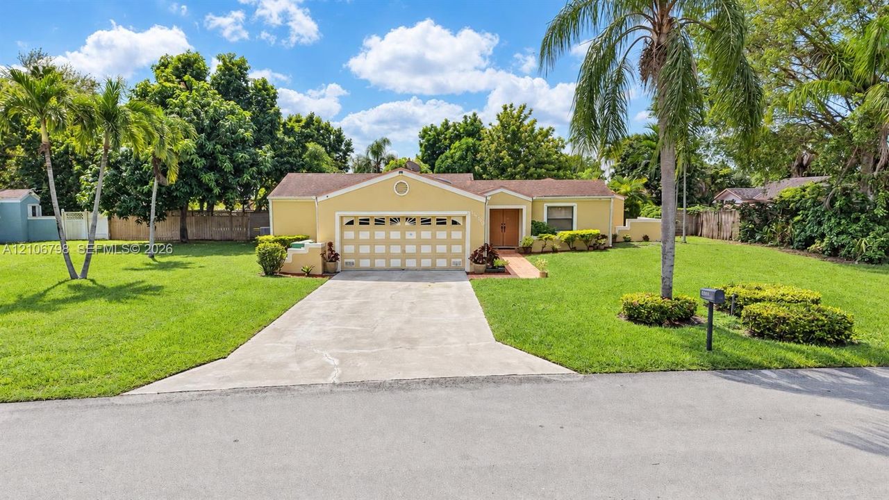 Single-story residence featuring a multi-car garage, concrete driveway, and expansive front lawn with mature palm trees