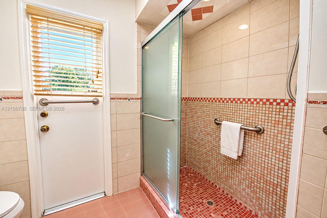Walk-in shower featuring a glass sliding door, mosaic tile detailing, wall-mounted safety grab bars, and neutral wall tile