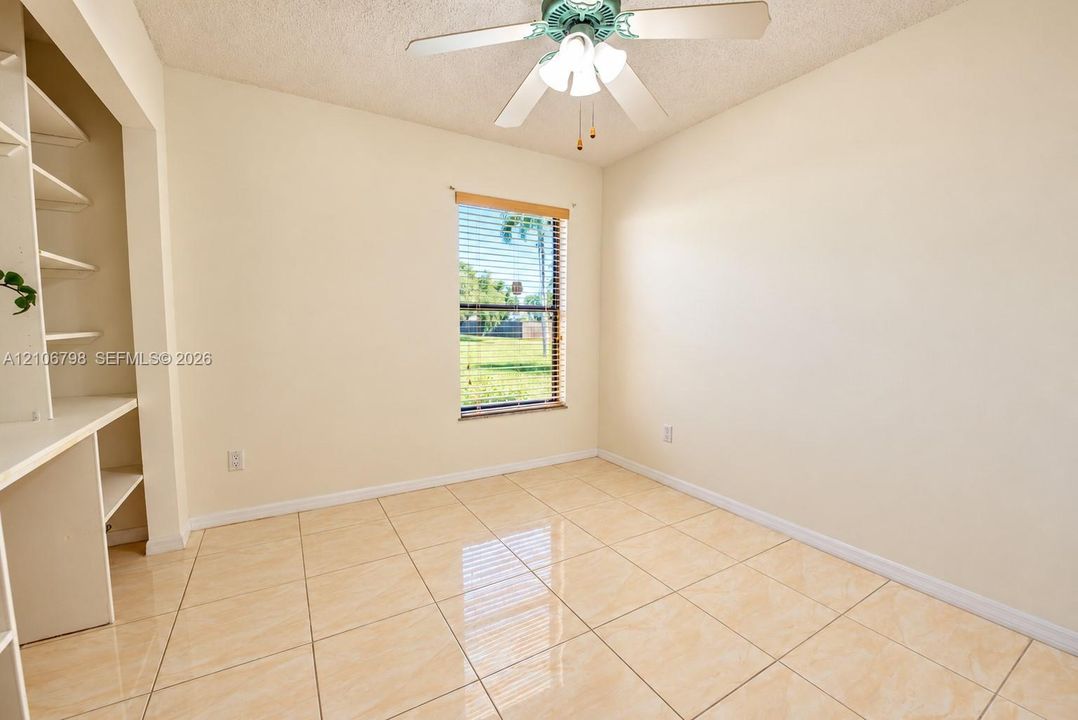 Room featuring large-format ceramic tile flooring, built-in shelving with an integrated desk, and a ceiling fan with integrated lighting