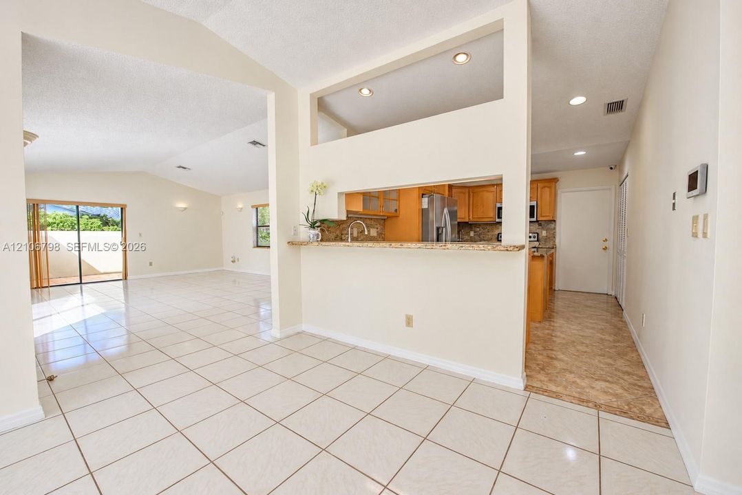 Interior space featuring tile flooring, vaulted ceilings, recessed lighting, a pass-through breakfast bar with stone-surfaced countertop, and natural light via sliding glass doors