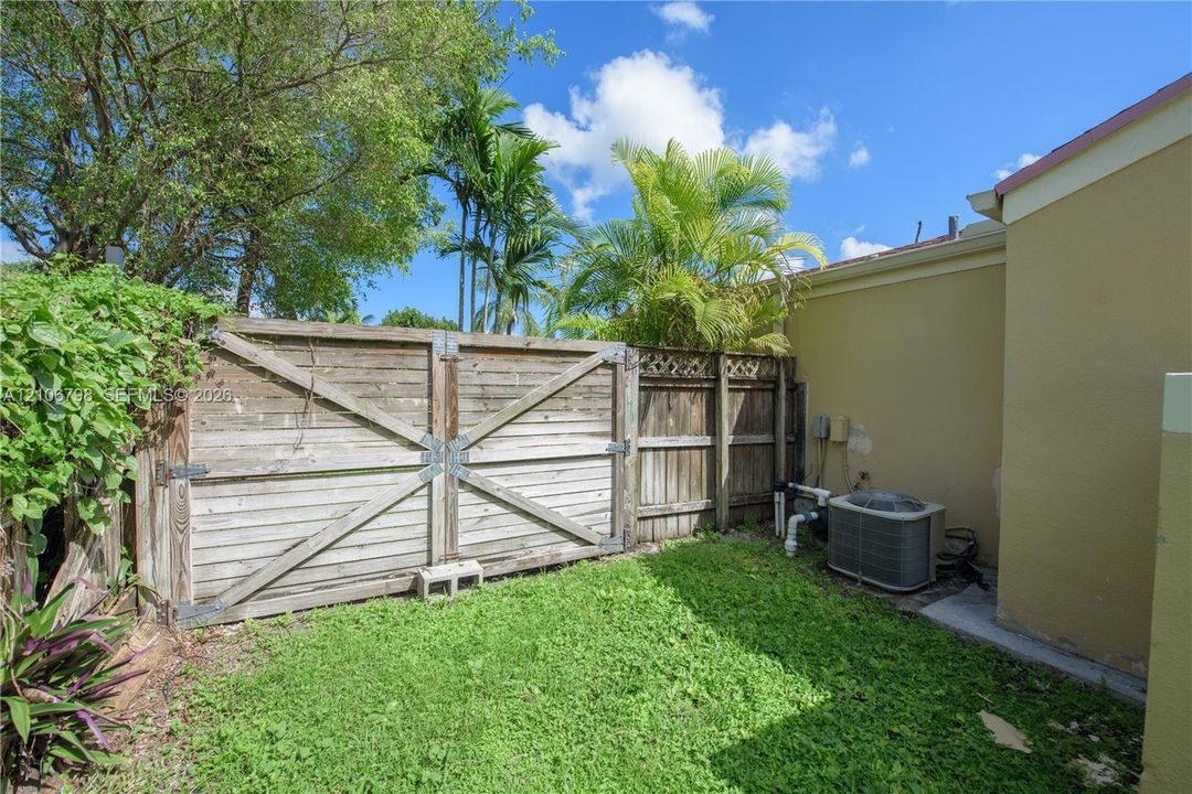 Side yard featuring a wood fence with metal hardware, mature palm trees, and an external HVAC unit