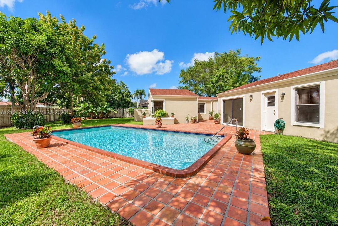 Rectangular swimming pool surrounded by a terracotta tile deck, manicured lawn, and mature perimeter trees