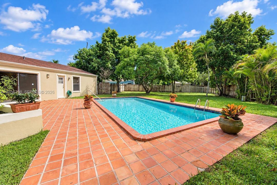 Private backyard featuring an in-ground swimming pool, terracotta tile patio, expansive lawn, mature trees, and perimeter fencing