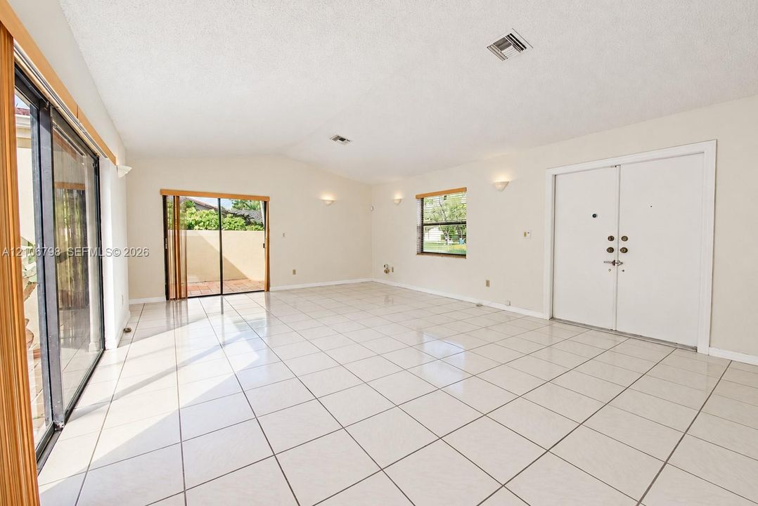 Interior space featuring large-format tile flooring, high vaulted ceilings, double-entry doors, dual sliding glass door systems, and wall-mounted sconce lighting