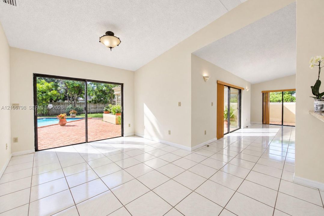 Interior space featuring light-colored tile flooring, vaulted ceilings, multiple sliding glass doors, flush-mount and wall-mounted lighting, and a private outdoor area with a swimming pool