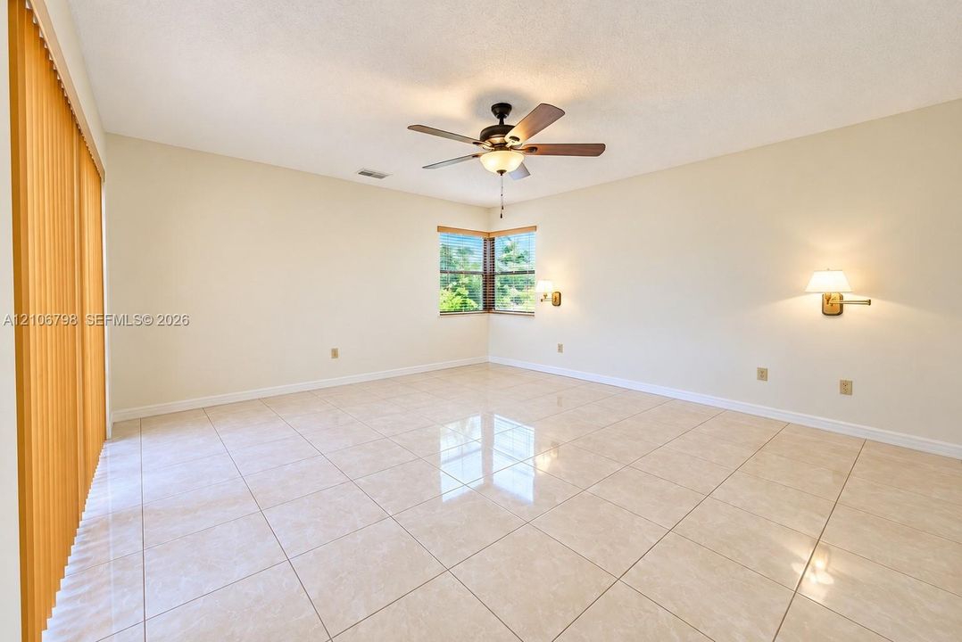 Neutral-toned ceramic tile flooring, ceiling fan with light fixture, wall-mounted swing-arm sconces, corner windows, and vertical blinds