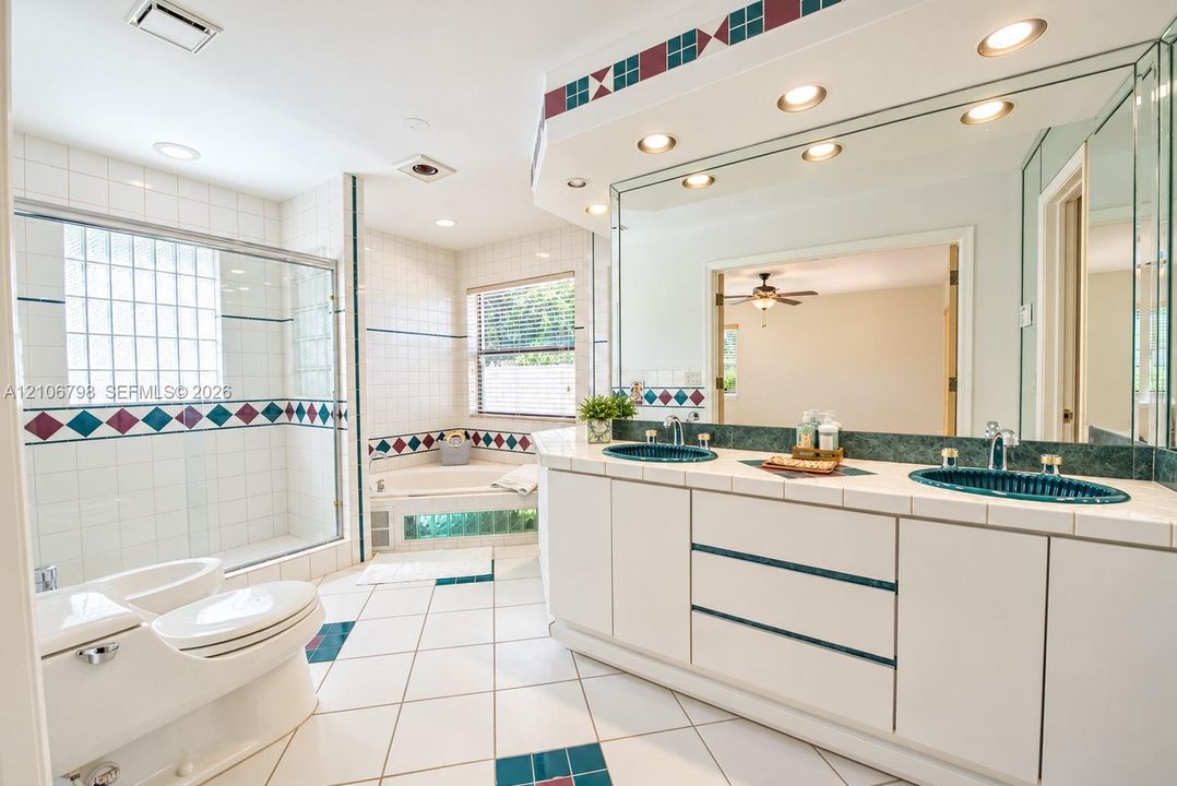 Dual-vanity cabinet featuring white cabinetry, tile countertop, and inset glass sinks with a large wall-to-wall mirror