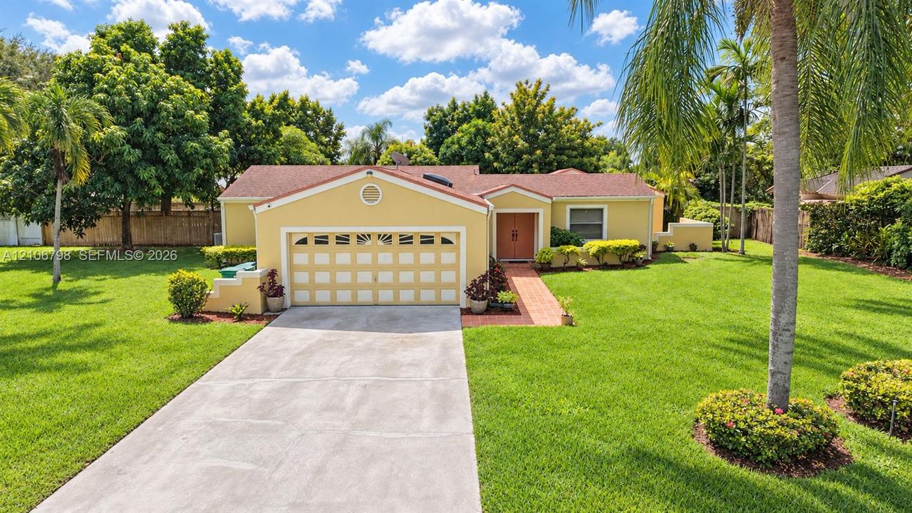 Single-story residence featuring a shingled roof, arched garage detailing, brick walkway, and extensive lawn landscaping with mature palms