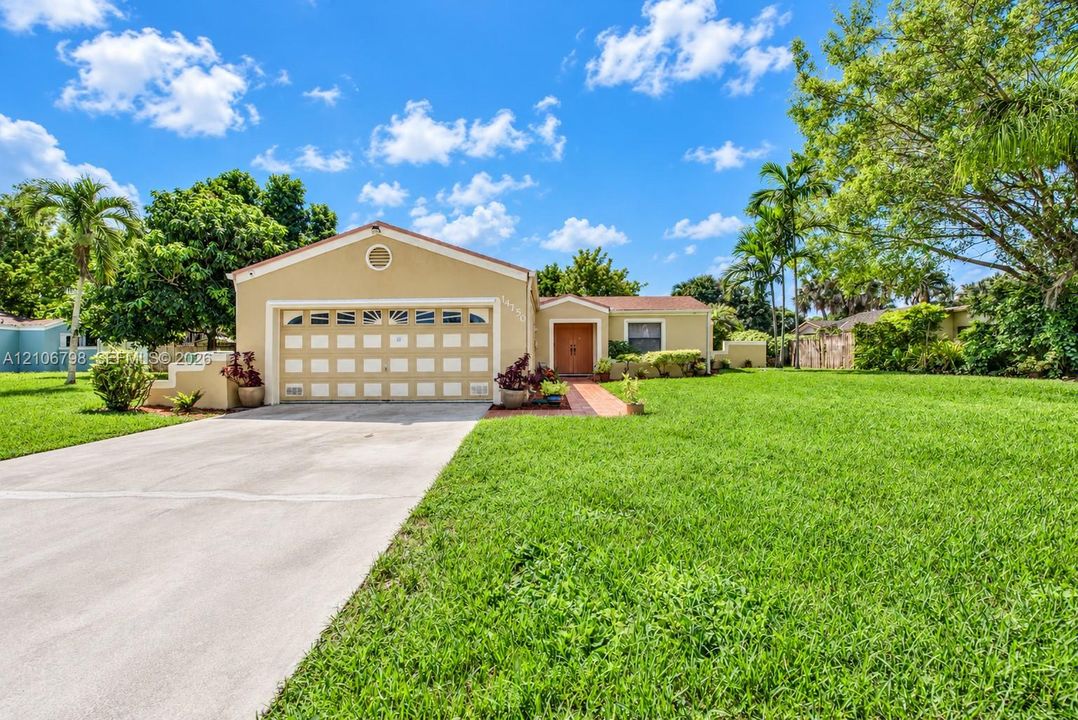 Single-story residence featuring a stucco exterior, multi-pane garage door, concrete driveway, and a paved walkway leading to the entrance, set on a property with mature landscaping