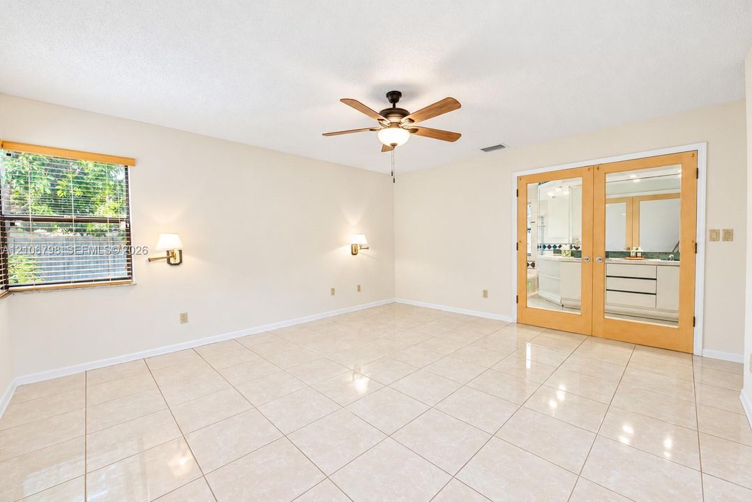 Neutral tile flooring, ceiling fan with light fixture, twin wall-mounted sconces, and wood-framed glass-paneled double doors