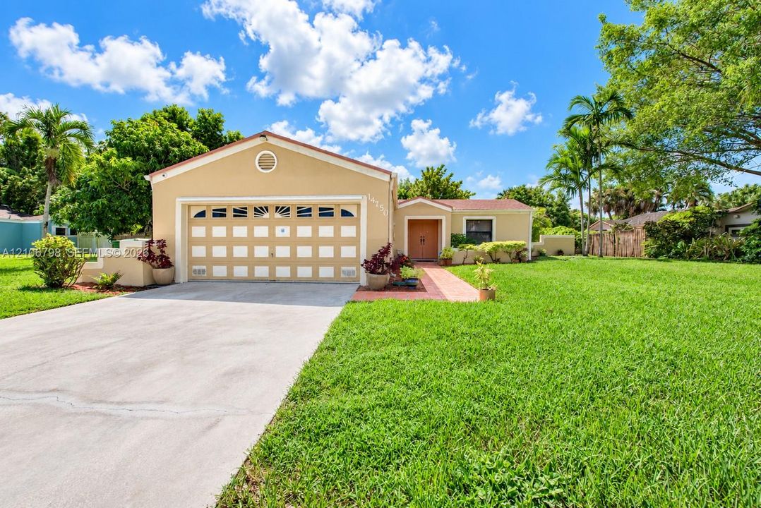 Stucco exterior featuring a two-car garage with arched decorative windows, concrete driveway, tiled entryway path, and expansive manicured lawn