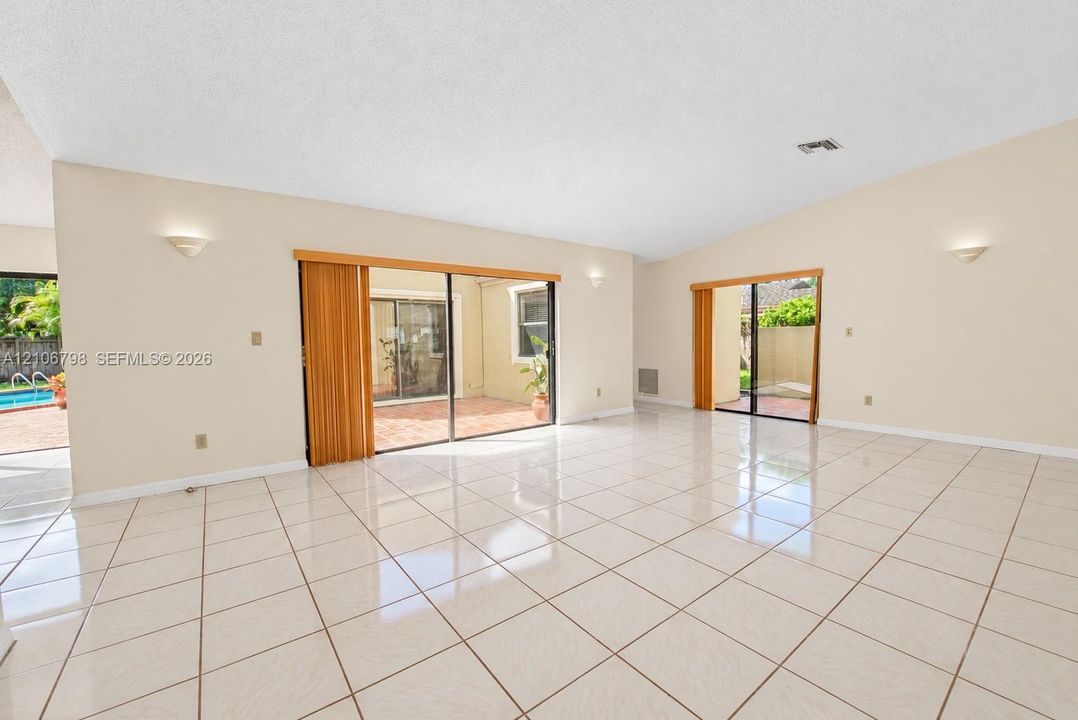 Spacious interior featuring vaulted ceilings, oversized ceramic tile flooring, dual sliding glass door systems, and wall-mounted sconce lighting