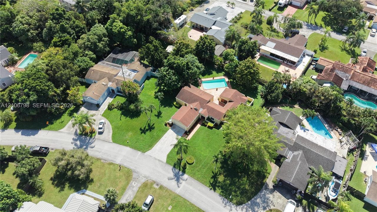 Aerial perspective of a multi-structure property featuring a pitched tile roof, expansive manicured lawn, concrete driveway, and a private swimming pool