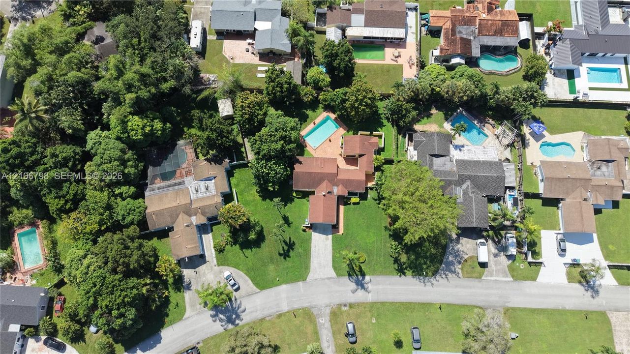 Aerial perspective of a property featuring a private swimming pool, terracotta-tiled patio, paved driveway, expansive lawn, and mature trees