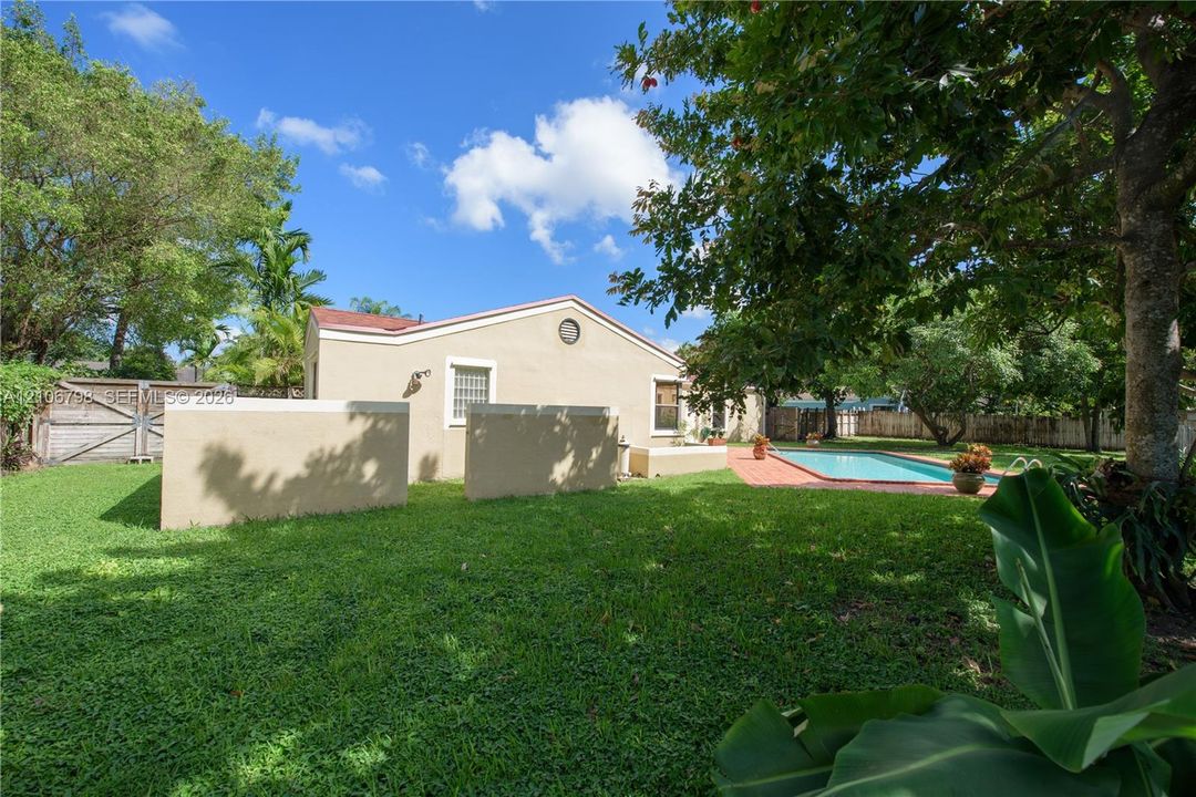 Expansive backyard featuring a manicured lawn, inground swimming pool, paved patio, perimeter wood fencing, and mature trees
