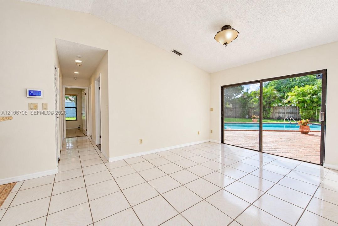 Vaulted ceiling, ceramic tile flooring, sliding glass doors, and direct exterior access to a private swimming pool with a brick-paved deck