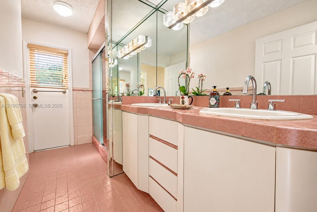 Double vanity featuring white cabinetry, tile countertops, integrated sinks, dual chrome faucets, and floor-to-ceiling mirror panels