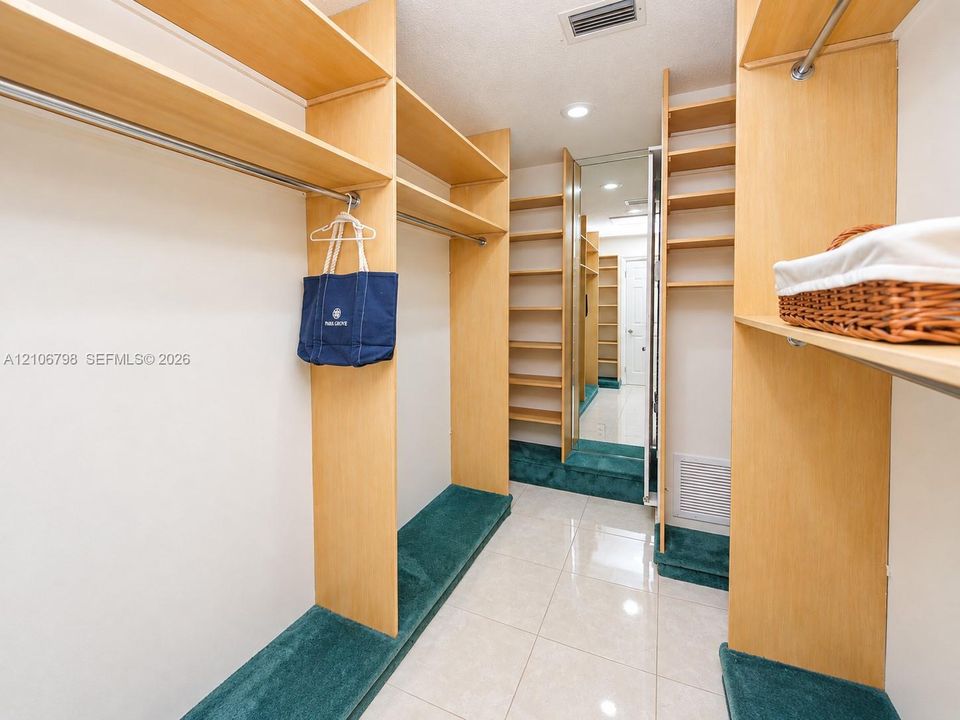 Custom storage system with light wood-finish shelving and metal garment rods, full-length mirror paneling, and tile flooring