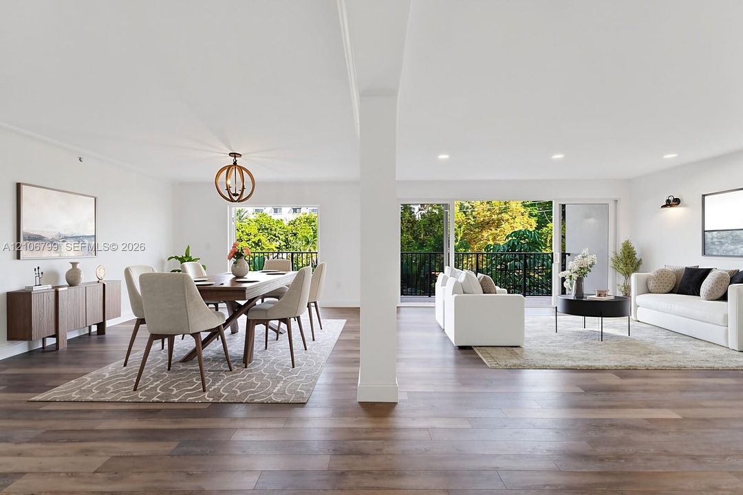 Open-concept living space featuring wood-finish flooring, recessed lighting, a structural support column, and dual sliding glass doors providing outdoor access to a railed balcony