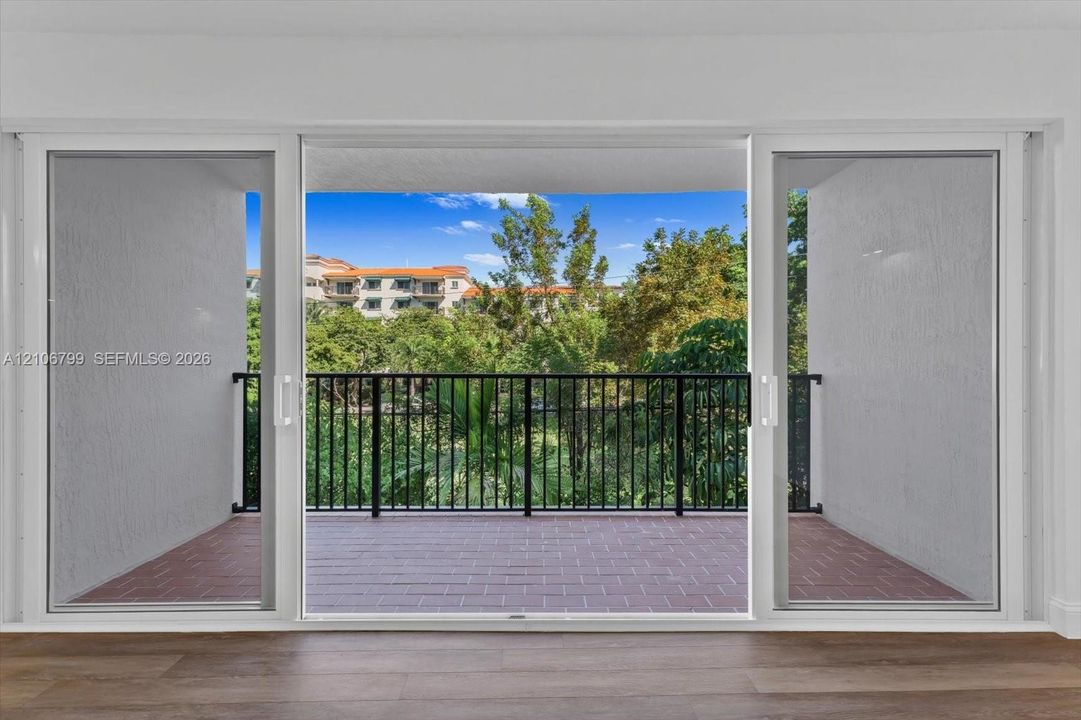 Large sliding glass doors opening to a covered balcony with brick-style flooring, a black metal railing, and wood-finish interior flooring