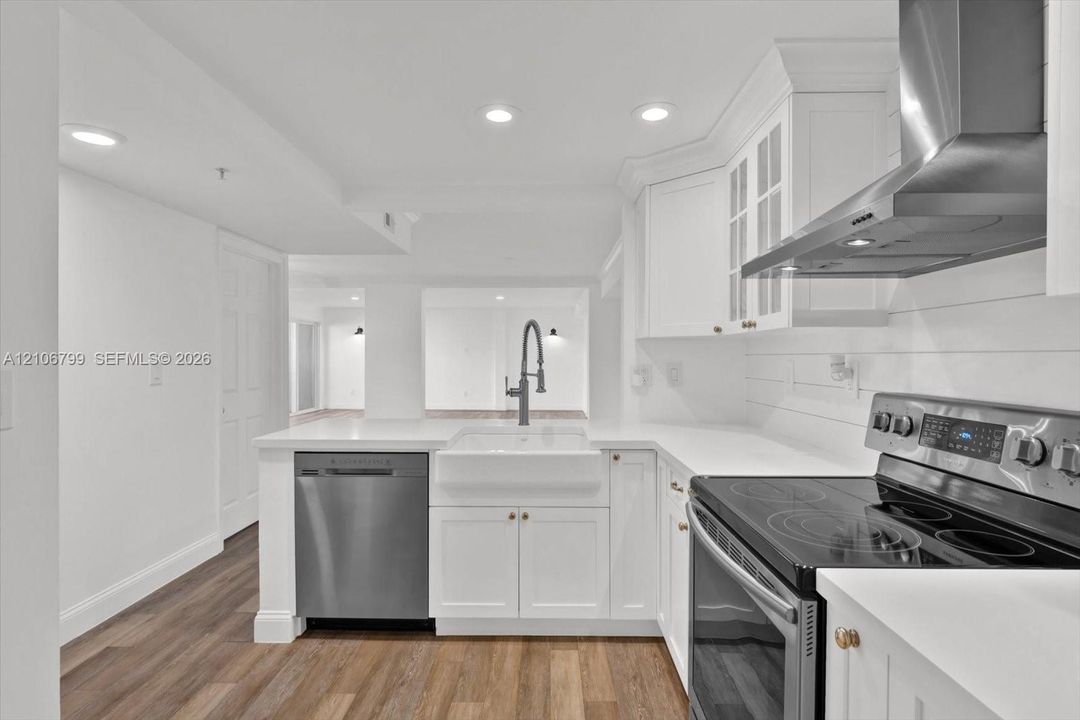 Kitchen featuring white shaker-style cabinetry, quartz countertops, a farmhouse-style sink with a gooseneck faucet, stainless steel appliances, and wood-finish flooring