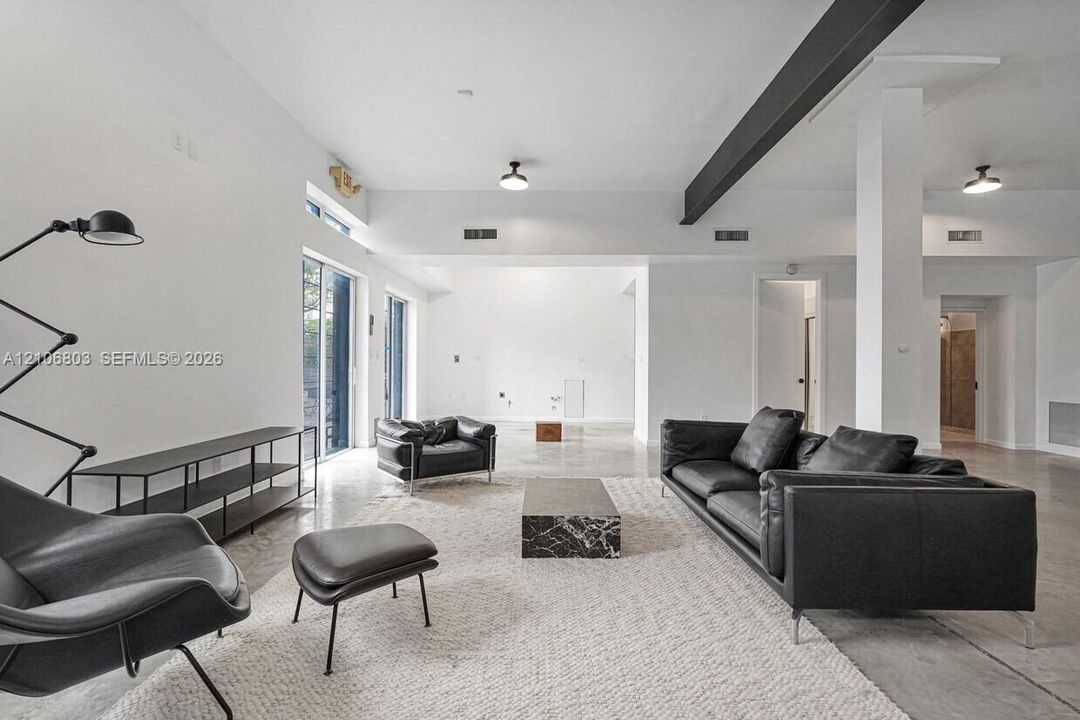 Open-concept interior featuring polished concrete flooring, high ceilings, exposed structural steel beam, and floor-to-ceiling glass sliding doors