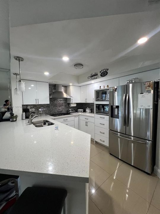 Kitchen featuring a stone-composite countertop, stainless steel appliances, gloss-finish cabinetry, tile flooring, and a glass-tile backsplash