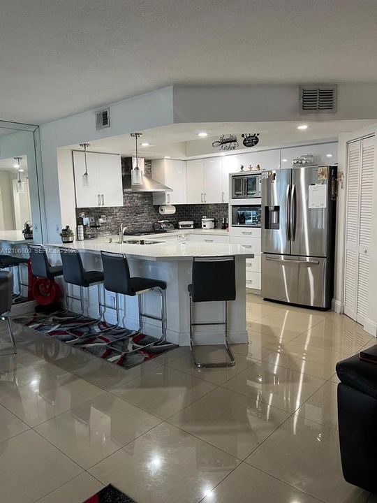Kitchen featuring white cabinetry, solid-surface countertops, stone-tile backsplash, stainless steel appliances, and large-format tile flooring