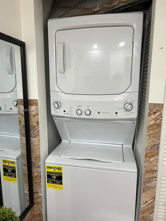 Stacked laundry unit with a white top-loading washer and front-loading dryer, situated within a built-in recessed enclosure featuring decorative stone-finish tile wall accents