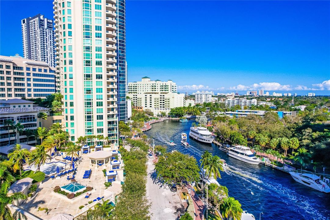 High-rise residential tower featuring glass-paneled balconies and exterior lighting, situated along a deep-water canal with a paved promenade and tropical landscaping