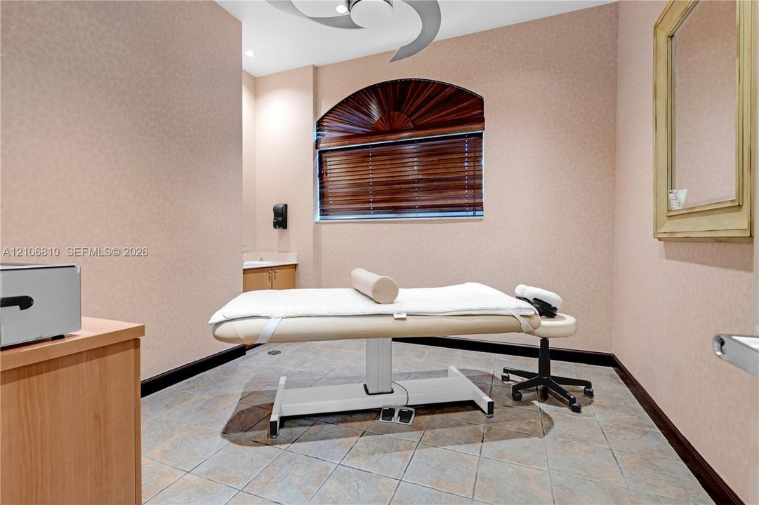 Arched window with wood-finish blinds, neutral wall surfacing, ceiling-mounted fan, tile flooring, and built-in cabinetry with sink