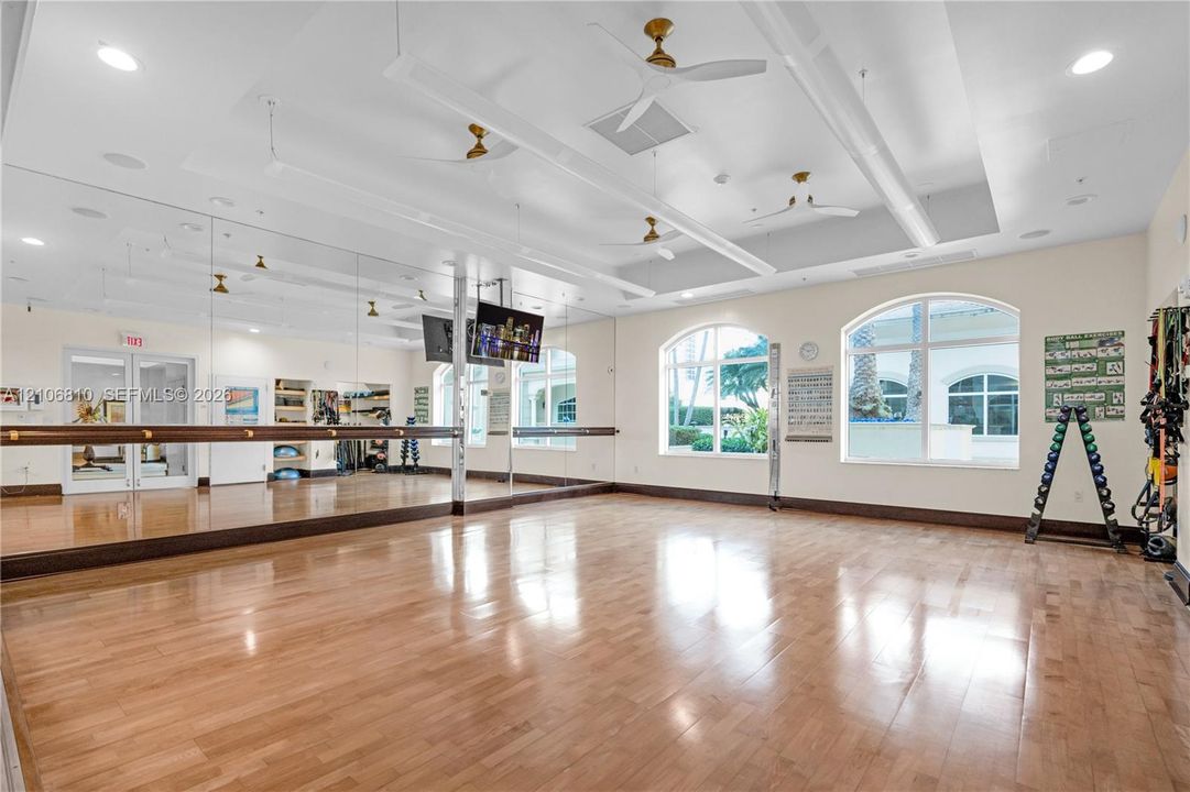 Spacious studio featuring wood-finish flooring, extensive wall-to-wall mirrors, recessed lighting, ceiling fans, and arched windows