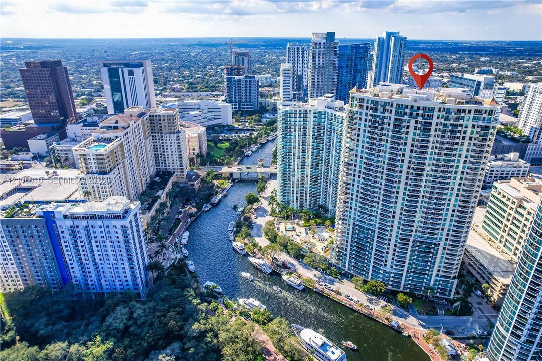 High-rise residential tower featuring a glass-facade exterior, multiple balconies, and a rooftop terrace situated along an urban waterway