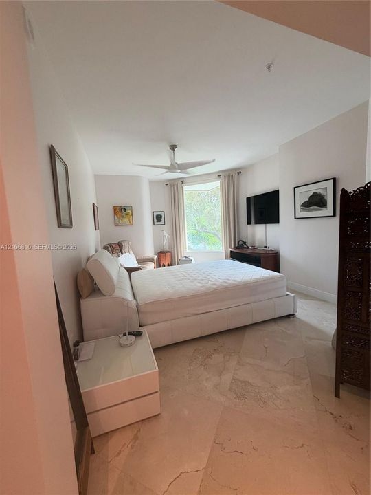 Spacious room featuring light-toned stone flooring, a ceiling fan, and a large bay window