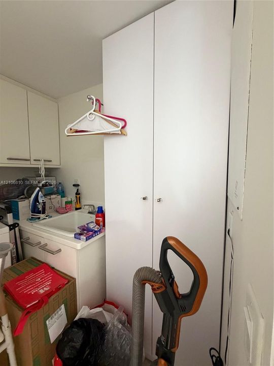 Tall white cabinetry with dual-door access, integrated wall-mounted upper cabinets, and a utility sink with a chrome faucet