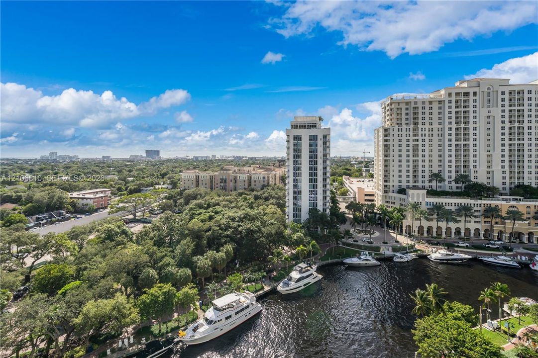 Aerial perspective of an urban waterway featuring moored yachts, mature canopy trees, and high-rise structures