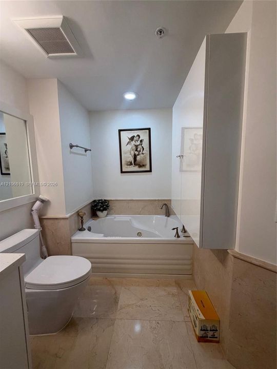 Bathroom featuring a built-in jetted soaking tub, stone tile flooring, matching stone wainscoting, and a white high-gloss wall-mounted cabinet