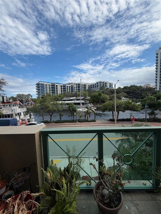 Exterior balcony featuring decorative metal railings and tile flooring, overlooking a waterway with surrounding greenery