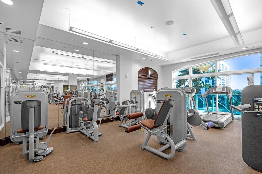Fitness center featuring full-wall mirrors, recessed lighting, multi-station exercise equipment, rubberized flooring, and large windows with exterior access