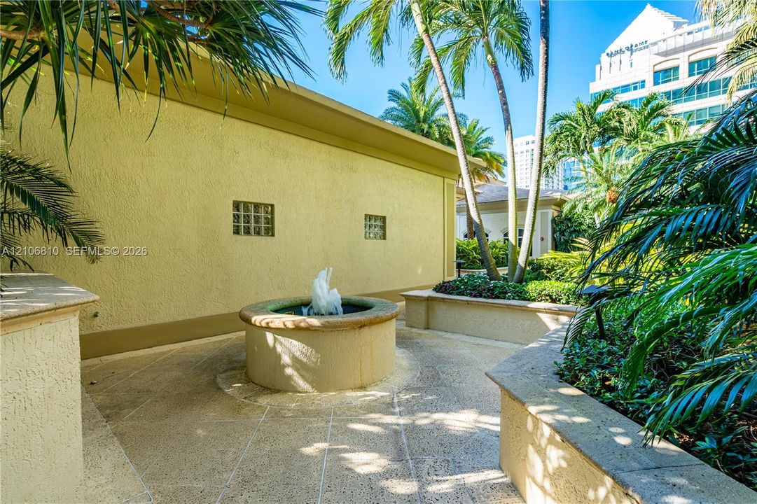 Outdoor courtyard featuring a central stone fountain, textured concrete patio, raised concrete masonry walls, and integrated glass block windows