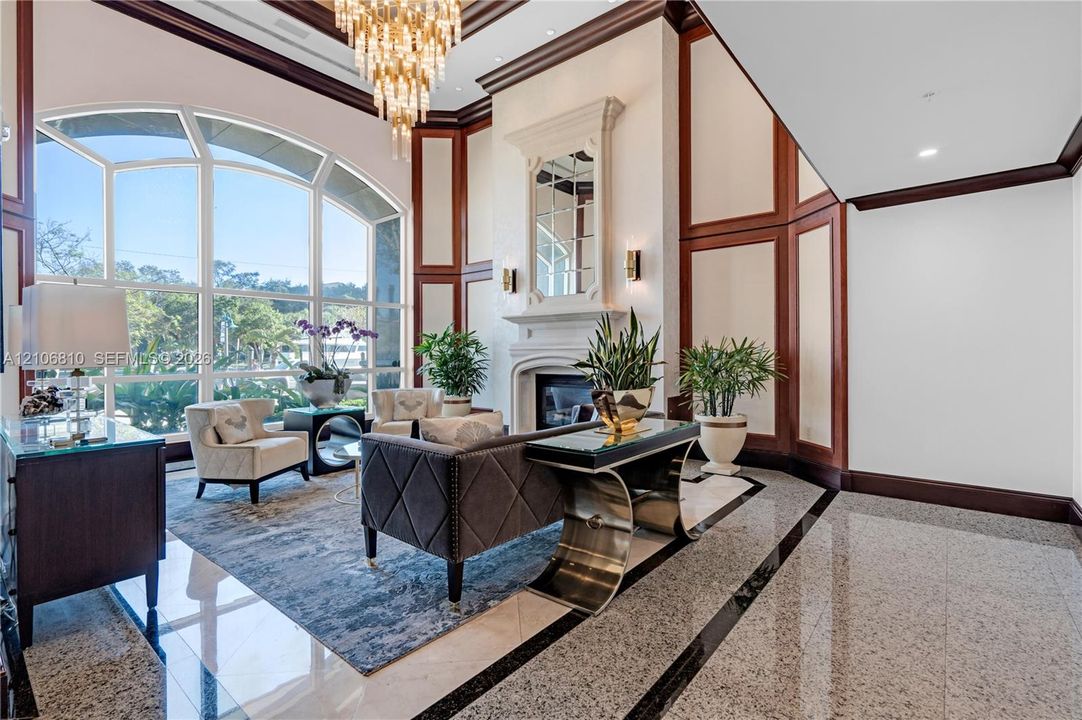 Grand foyer featuring expansive arched windows, polished stone flooring, intricate wood-paneled walls, a fireplace with an integrated mirror, and a decorative tiered chandelier