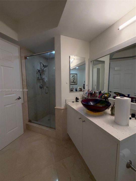 Bathroom featuring a solid-surface vanity countertop, vessel sink, walk-in shower with a glass enclosure, large wall-mounted mirror, and stone-tile flooring