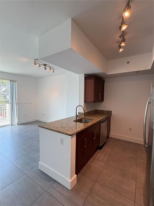 Kitchen featuring wood cabinetry, stone countertops, an undermount stainless steel sink with a high-arch faucet, large-format tile flooring, and multi-directional track lighting