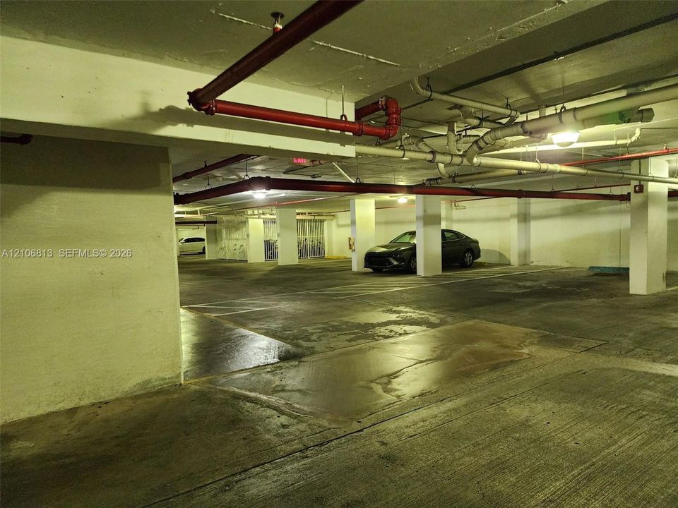 Enclosed parking garage featuring concrete flooring, structural support pillars, and ceiling-mounted fire suppression systems