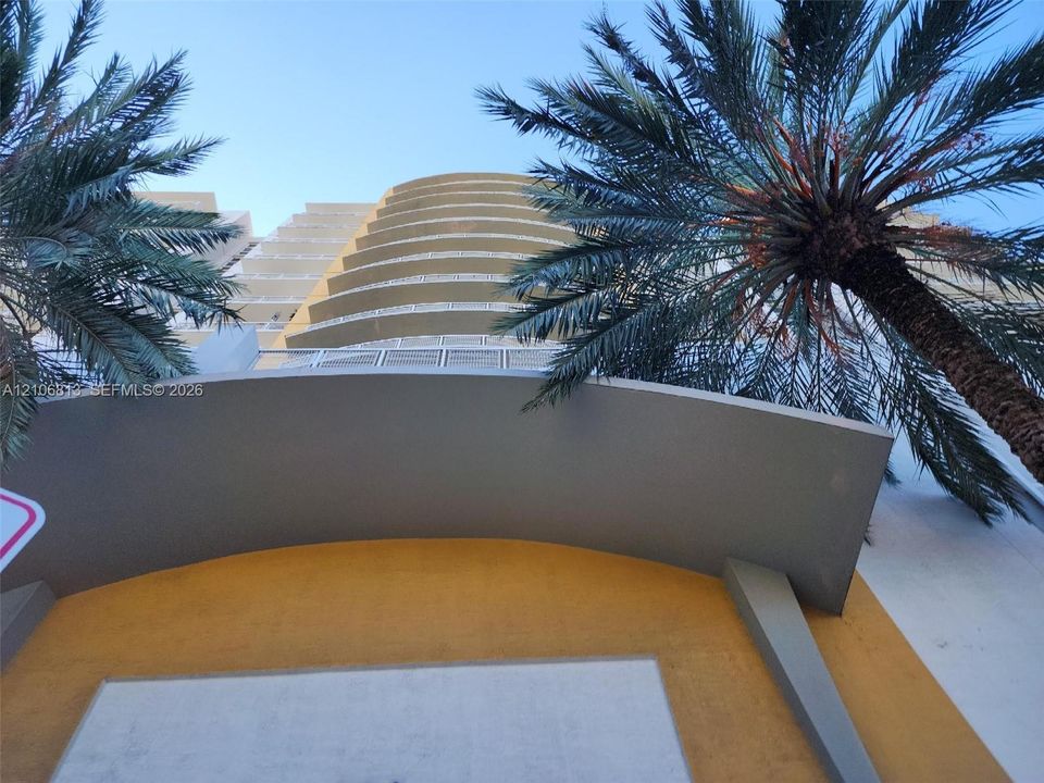 Multi-story residential exterior featuring private cantilevered balconies with white grid-pattern metal railings and textured stucco facade