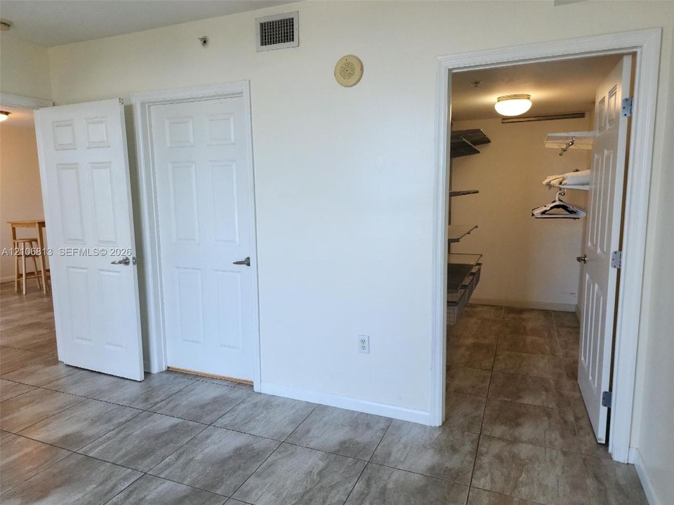 Large-format tile flooring throughout featuring a neutral stone pattern, walk-in closet with custom built-in shelving, and six-panel interior doors