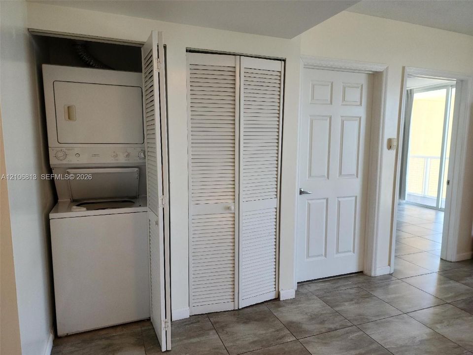 Stacked laundry unit, white louvered closet doors, and ceramic tile flooring