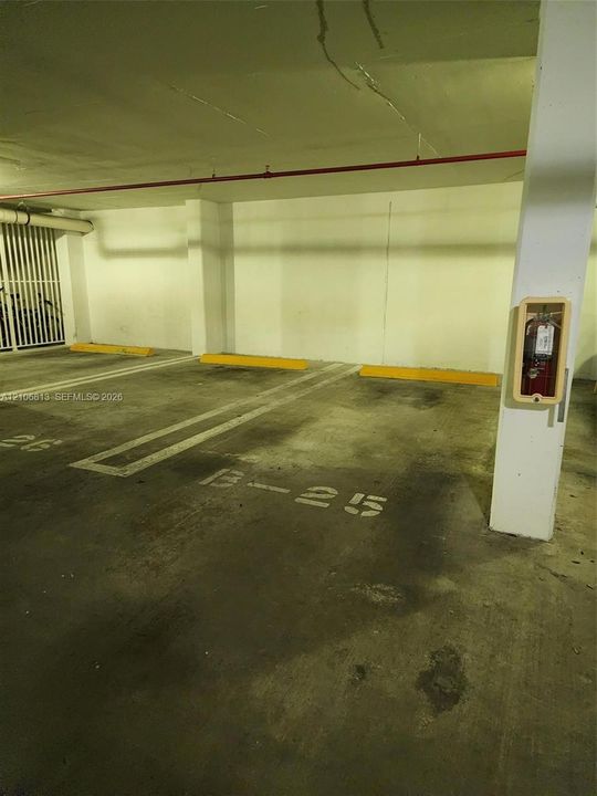 Covered parking area featuring concrete flooring, designated numbered spaces, yellow wheel stops, and a mounted fire extinguisher