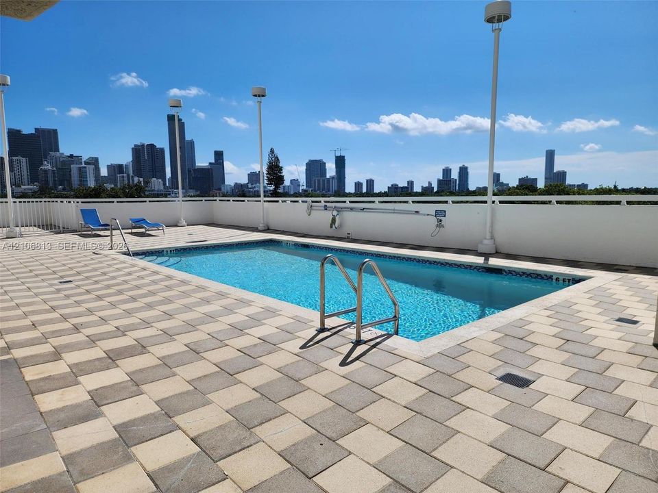 Rooftop swimming pool featuring a tiled deck, perimeter safety railing, built-in pool ladder, and urban skyline backdrop
