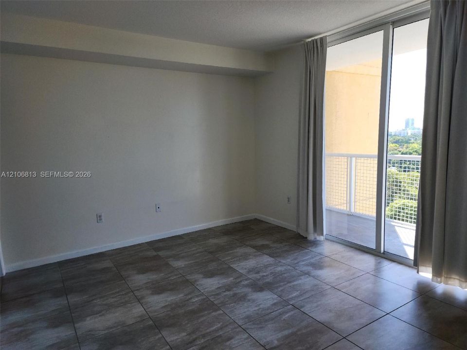Neutral-toned interior space featuring large-format ceramic tile flooring and full-height sliding glass doors opening to an exterior balcony with a white metal railing